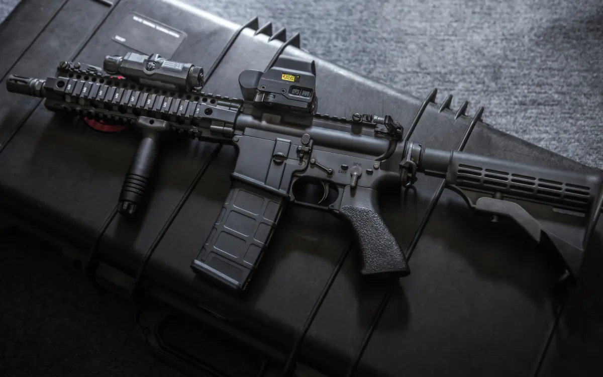 A carbine fitted with two electronic sights on a dark equipment case